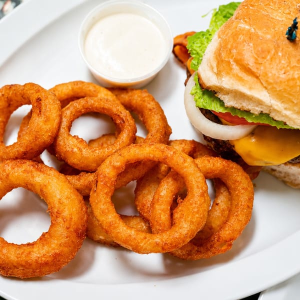 A cheeseburger with lettuce, tomato, and onion, served with crispy onion rings and a side of dipping sauce.