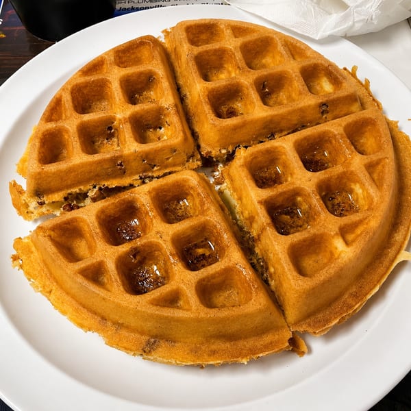 Golden-brown waffle, cut into four pieces, drizzled with syrup on a white plate.
