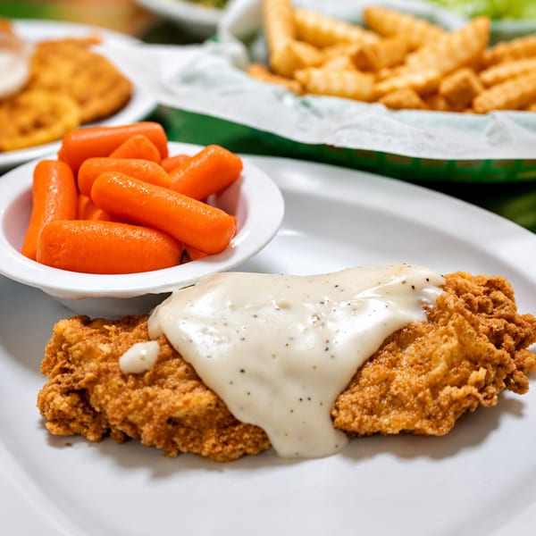 Chicken fried steak with gravy, a side of baby carrots, and a basket of fries.