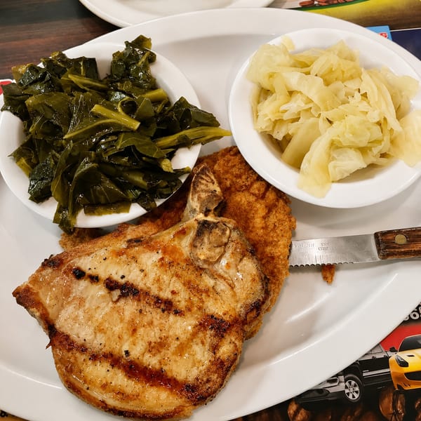 Grilled pork chop, fried chicken, collard greens, and cabbage on a white plate with a knife.