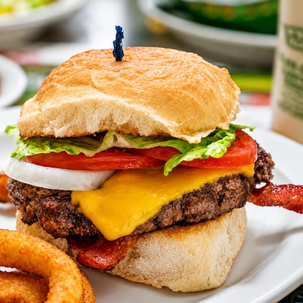 A cheeseburger with bacon, lettuce, tomato, and onion, served with onion rings.